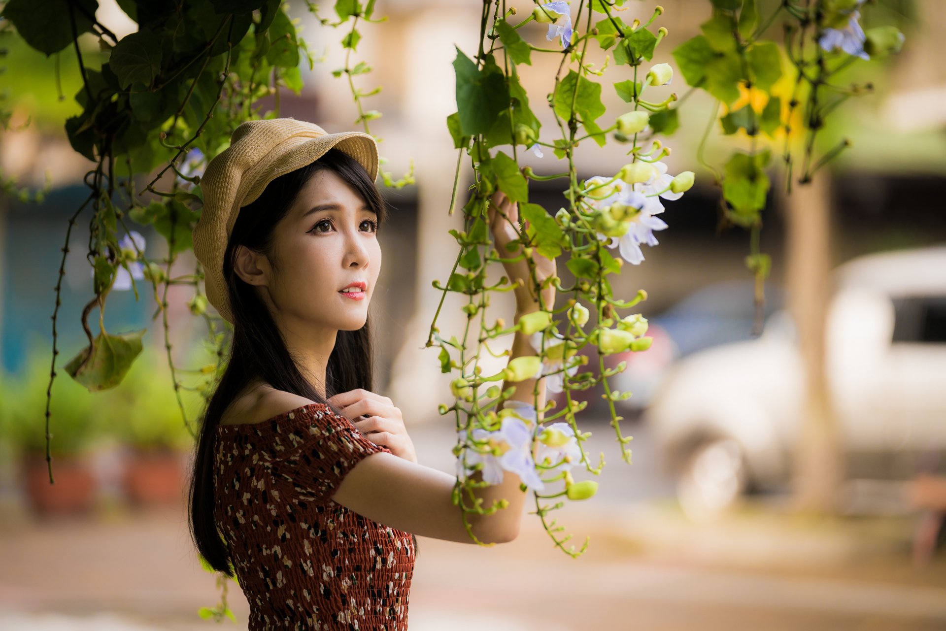 4K Ultra HD PC desktop wallpaper: a woman model with long black hair and a sun hat reaching toward hanging flowers, shallow depth-of-field with soft bokeh background