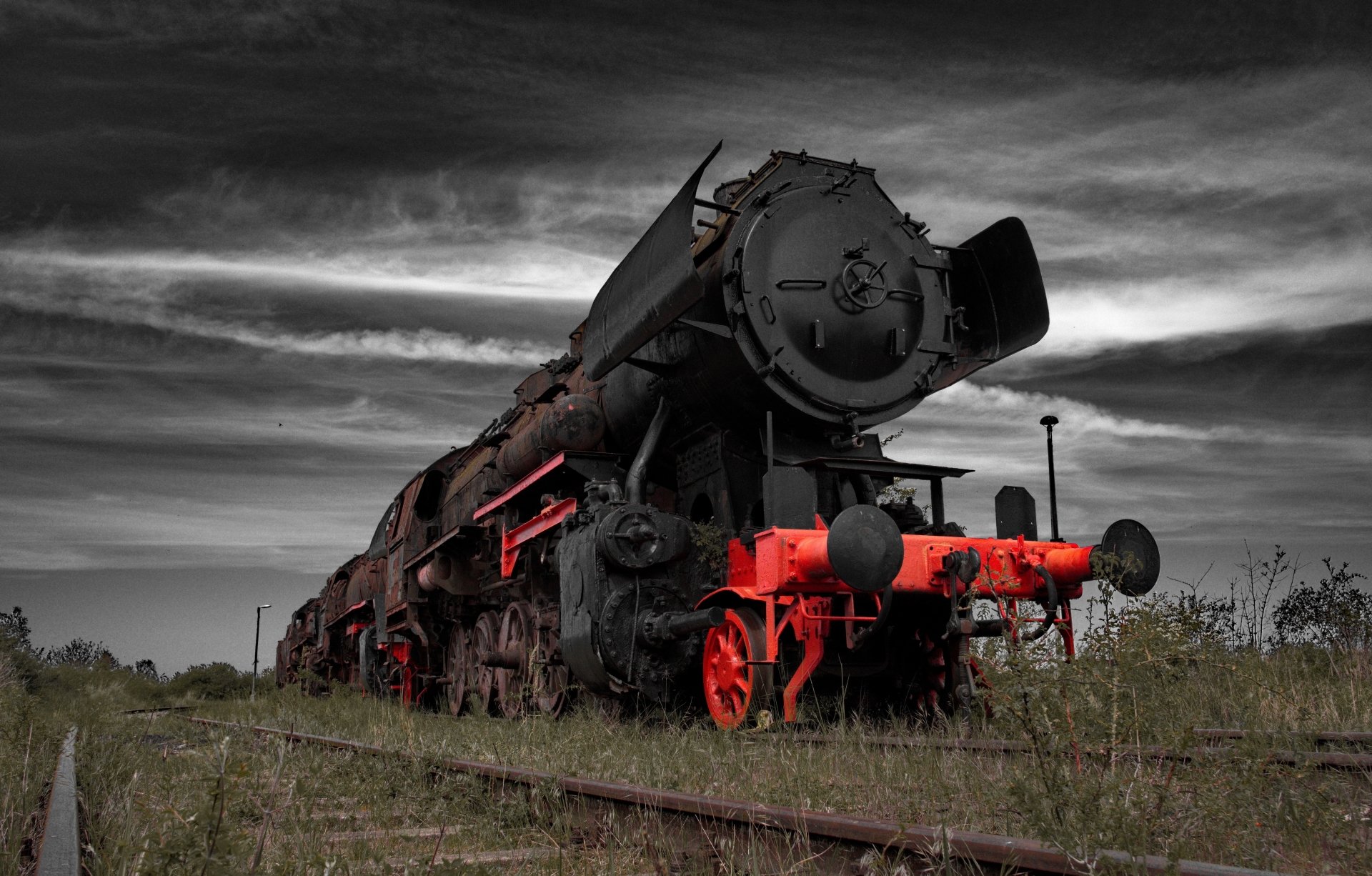 5K Ultra HD PC desktop wallpaper of a vintage steam locomotive vehicle with bright red front, sitting on overgrown tracks beneath a dramatic cloudy sky.