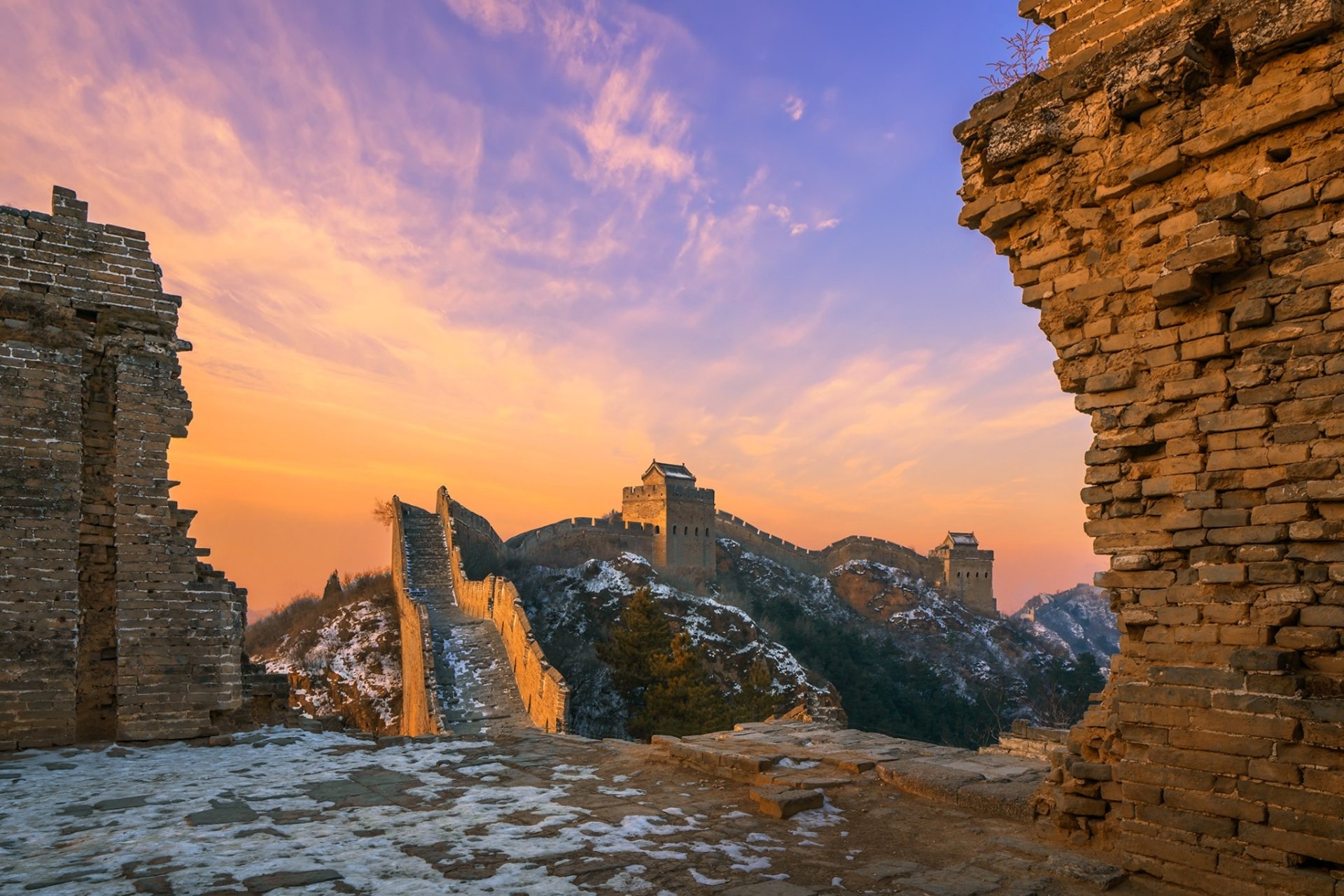 HD desktop wallpaper showcasing the man-made Great Wall of China winding over rugged hills at sunset, framed by ancient stone ruins.