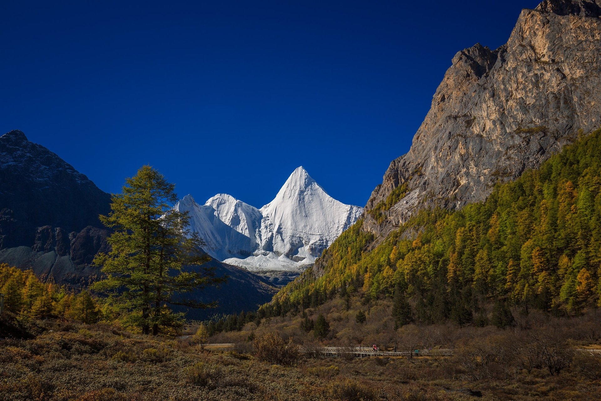 HD PC desktop wallpaper and background: China mountain nature scene with a snow-capped peak between rocky cliffs and golden autumn forest under a deep blue sky.
