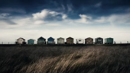 A row of colorful huts under a dramatic cloudy sky, captured in stunning 4K Ultra HD landscape photography, set against tall grasses in the foreground.