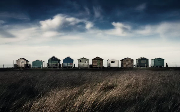 A row of colorful huts under a dramatic cloudy sky, captured in stunning 4K Ultra HD landscape photography, set against tall grasses in the foreground.