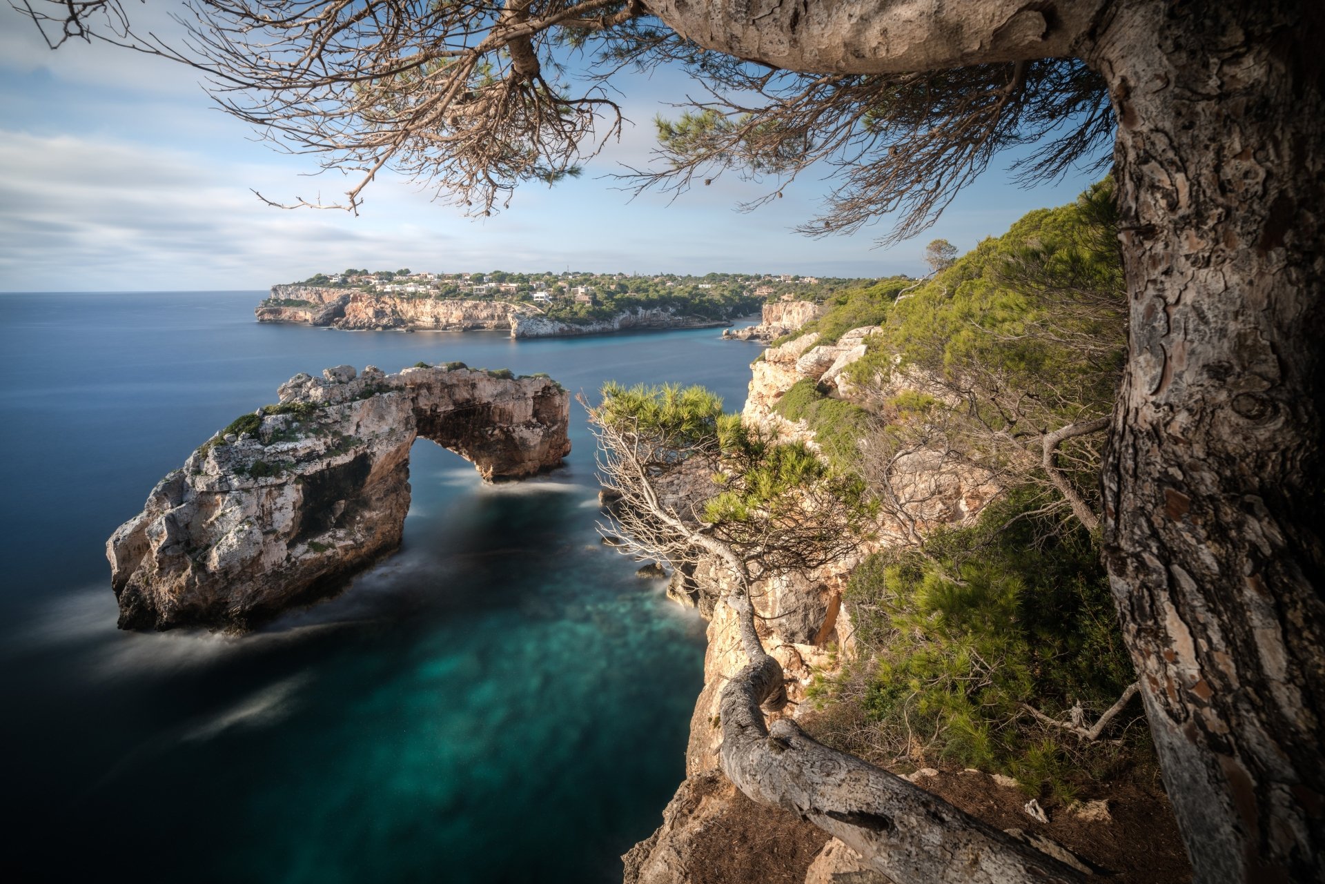 4K Ultra HD PC desktop wallpaper: coastal nature scene with a rocky arch over turquoise water, cliffs and windswept pines under a blue sky.