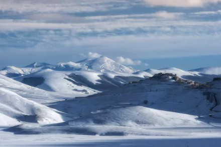 Snow-covered mountains under a partly cloudy sky in Umbria, Italy, captured in stunning 4K Ultra HD winter landscape photography.