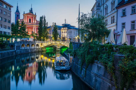HD PC desktop wallpaper of Ljubljana, Slovenia: evening city river view with boat, arched bridge, church steeples and man-made riverside buildings.