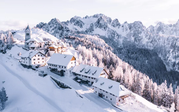 Snow-covered lodge and houses nestled in a mountain village with frosted trees and towering snowy peaks in the background, captured in crisp 4K Ultra HD winter photography.