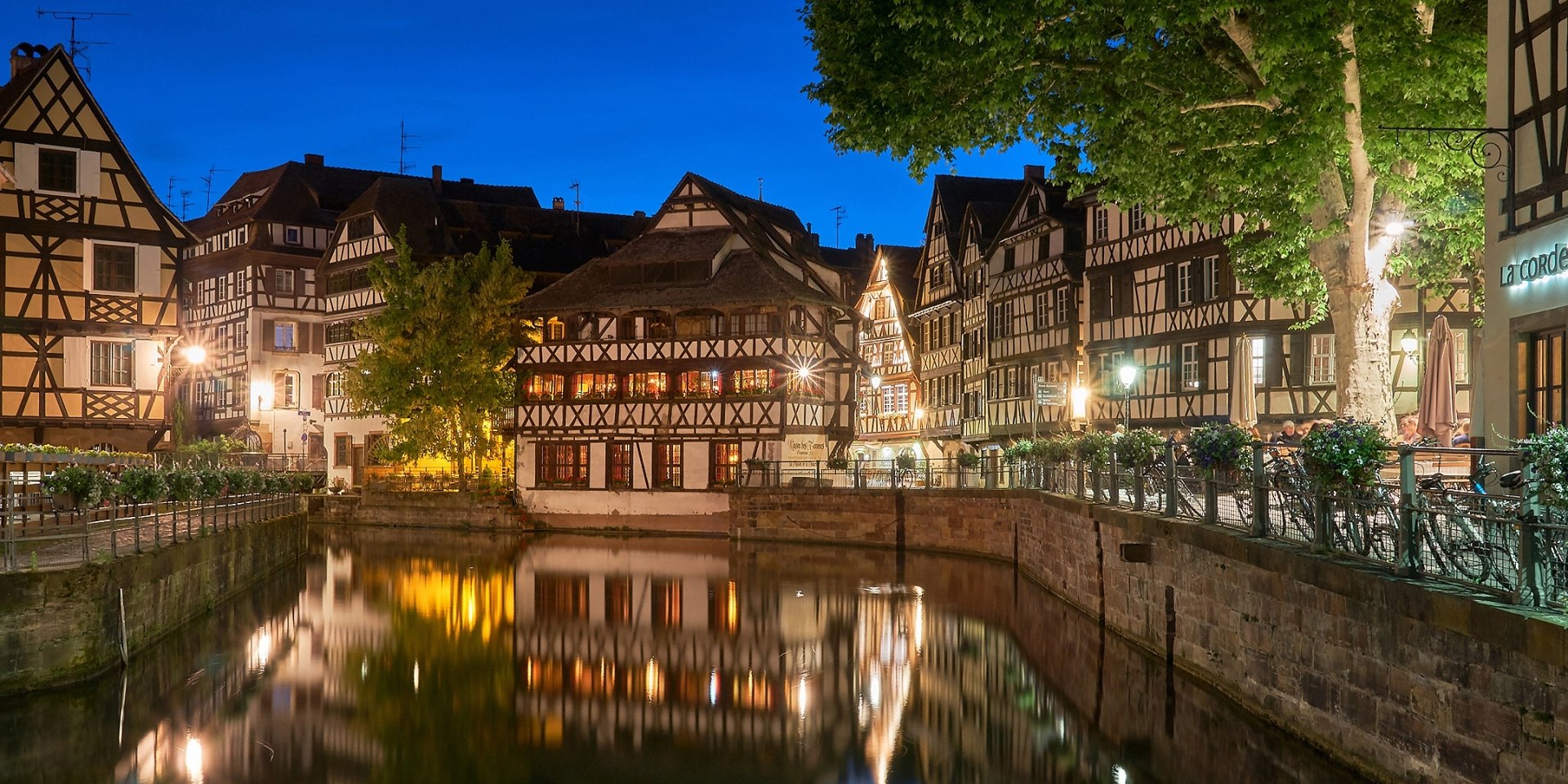 Night view of historic half-timbered houses along a canal in Strasbourg, France, with clear reflections on the water.