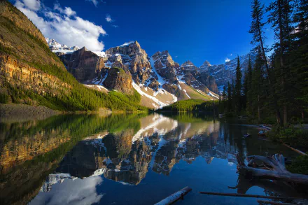 Moraine Lake in Banff National Park, Alberta, Canada, reflects towering snow-capped mountains and surrounding pine trees on its clear, calm waters.