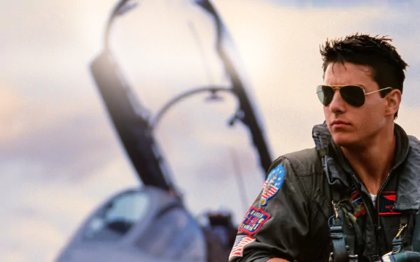 Tom Cruise as a pilot in Top Gun, wearing aviator sunglasses and flight suit, standing beside a fighter jet in this 4K Ultra HD PC desktop wallpaper.