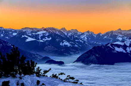 Snow-covered Bernese Alps in Switzerland at sunset with vibrant orange sky above mountainous peaks and a blanket of clouds below, captured in HD.