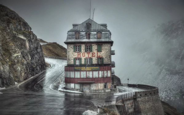 HD desktop wallpaper featuring a man-made hotel nestled at a mountain road junction, surrounded by misty peaks and winding pavement.