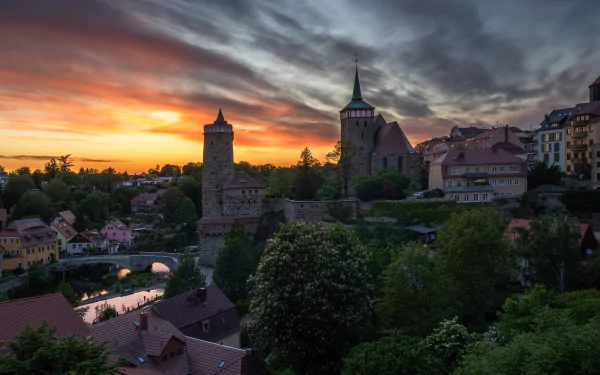 Evening view of a German riverside town with a stone fortress and tower, houses along the river under dramatic sunset clouds — 5K Ultra HD PC desktop wallpaper.
