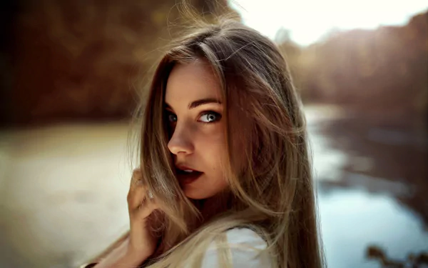4K Ultra HD PC desktop wallpaper: close-up portrait of a woman's face with long hair, intense eyes and a contemplative expression, soft blurred background by water.
