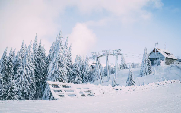 4K Ultra HD PC desktop wallpaper: a photographic winter scene of snow-laden fir trees, a wooden fence, clouds overhead, a cabin and ski lift framed in pristine snow.