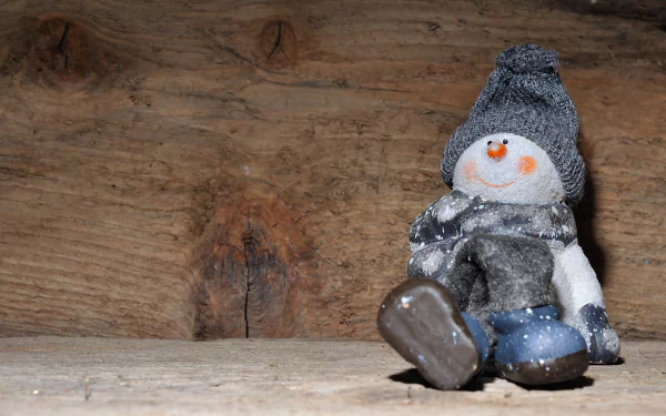 Snowman figurine in a knit hat and scarf sits on a rustic wooden plank, Christmas photography — 4K Ultra HD PC desktop wallpaper and background.