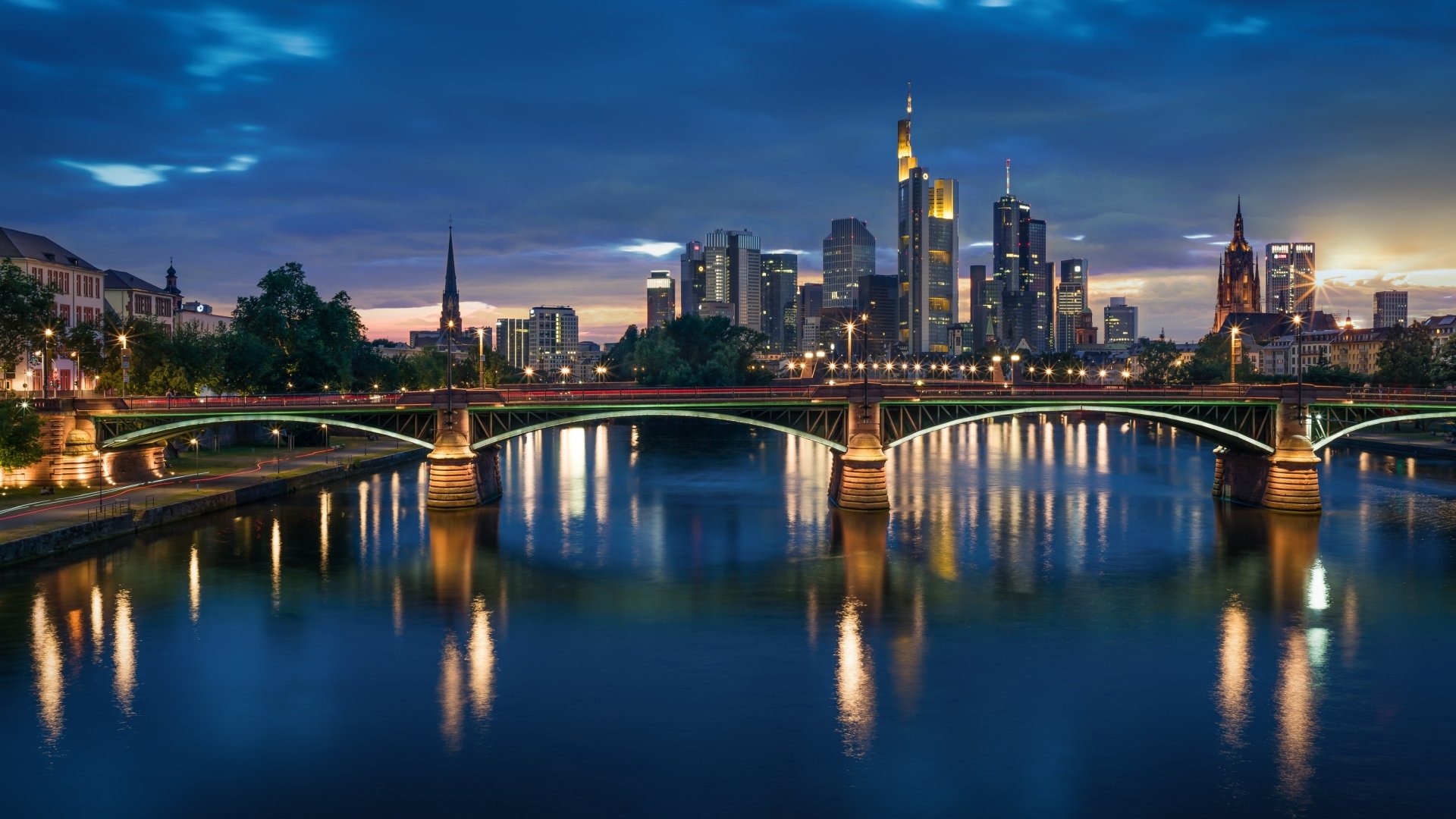 Frankfurt, Germany at night — illuminated man-made bridge over a reflective river with the city skyline, rendered as a 2K Quad HD PC desktop wallpaper.