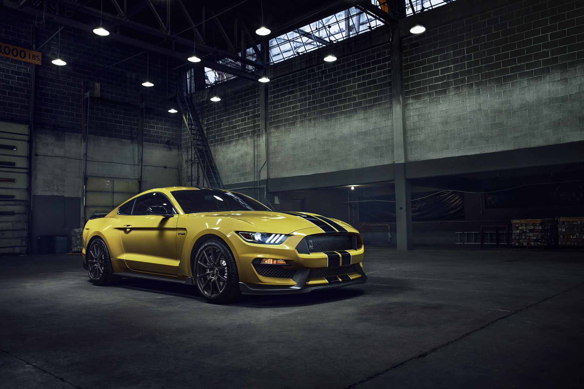 A yellow Ford Mustang GT350 muscle car parked inside a dimly lit industrial garage, captured in 4K Ultra HD for a PC desktop wallpaper.