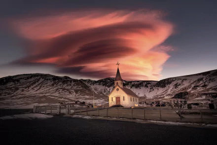 5K Ultra HD PC desktop wallpaper: illuminated Icelandic church at dusk, a religious white chapel among snowy hills beneath dramatic swirling pink clouds.