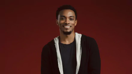 HD desktop wallpaper and background featuring a smiling man in a black shirt with a white cardigan against a red backdrop.