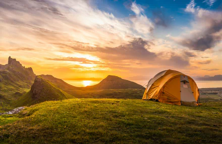HD wallpaper of a scenic camping setup with a tent on a hillside at sunset.