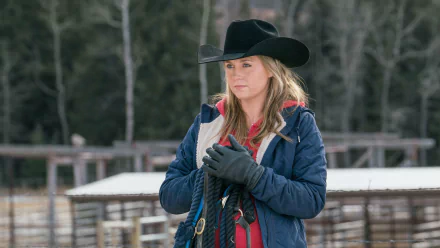 A scene from the TV show Heartland featuring a young woman in a cowboy hat, holding ropes, set against a rustic farm background. This HD wallpaper captures the essence of ranch life.
