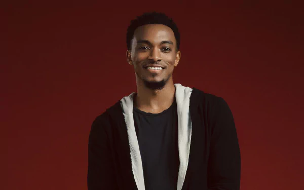HD desktop wallpaper and background featuring a smiling man in a black shirt with a white cardigan against a red backdrop.