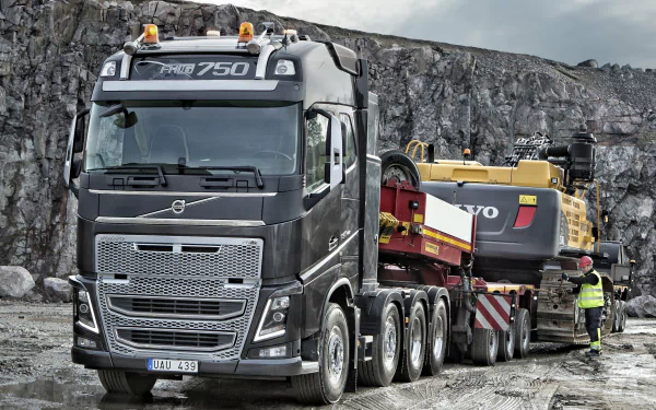 A Volvo FH16 750 truck hauling heavy equipment, set as a high-definition desktop wallpaper with a rugged quarry backdrop.