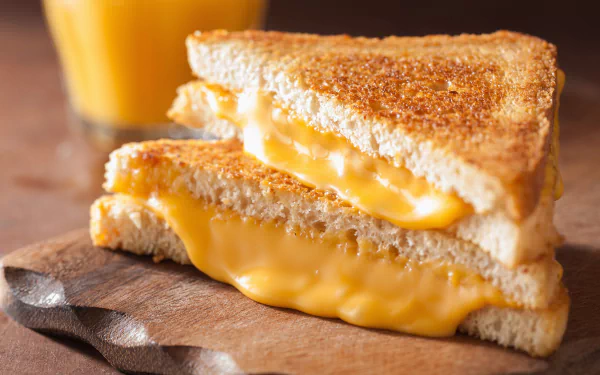 HD wallpaper of a delicious grilled cheese sandwich on a wooden board with a glass of juice in the background.