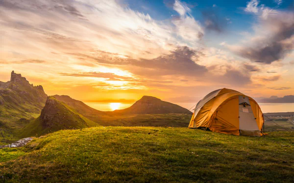 HD wallpaper of a scenic camping setup with a tent on a hillside at sunset.