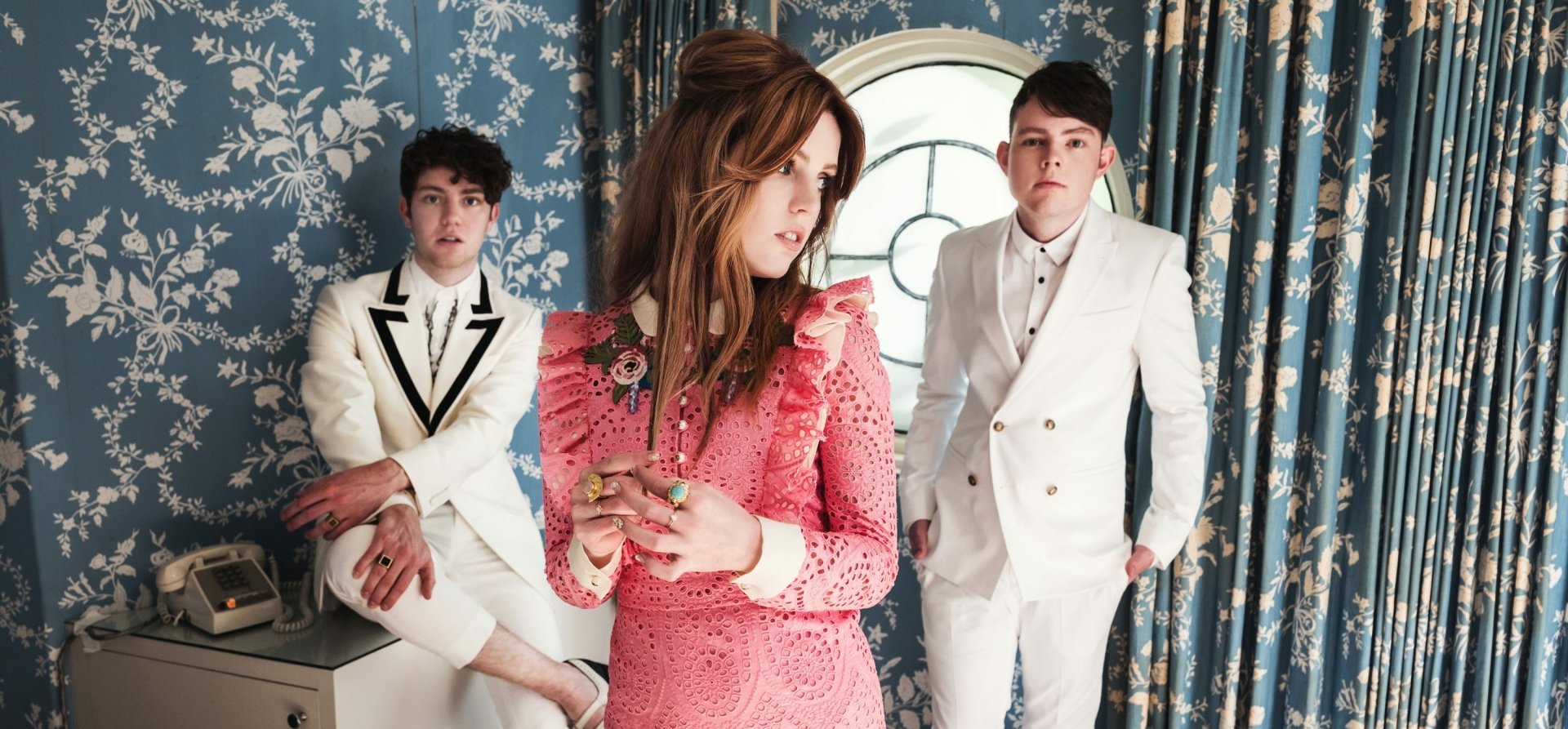 HD desktop wallpaper featuring the band Echosmith with Sydney Sierota in the foreground, standing in a room with vintage wallpaper.