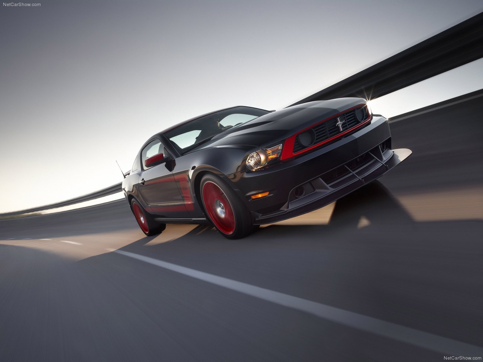 Sleek black Ford Mustang Boss 302 with red accents speeding on a curved highway, captured in an HD PC desktop wallpaper background.