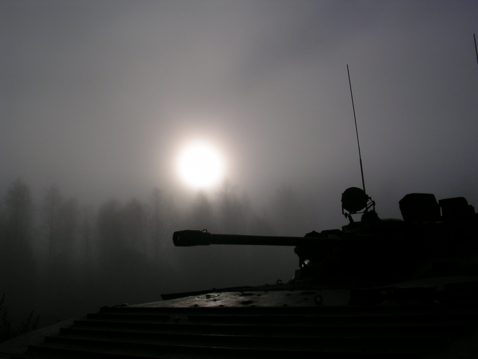 HD desktop wallpaper featuring a military tank silhouette against a misty backdrop with the sun rising, casting a serene glow through the fog.