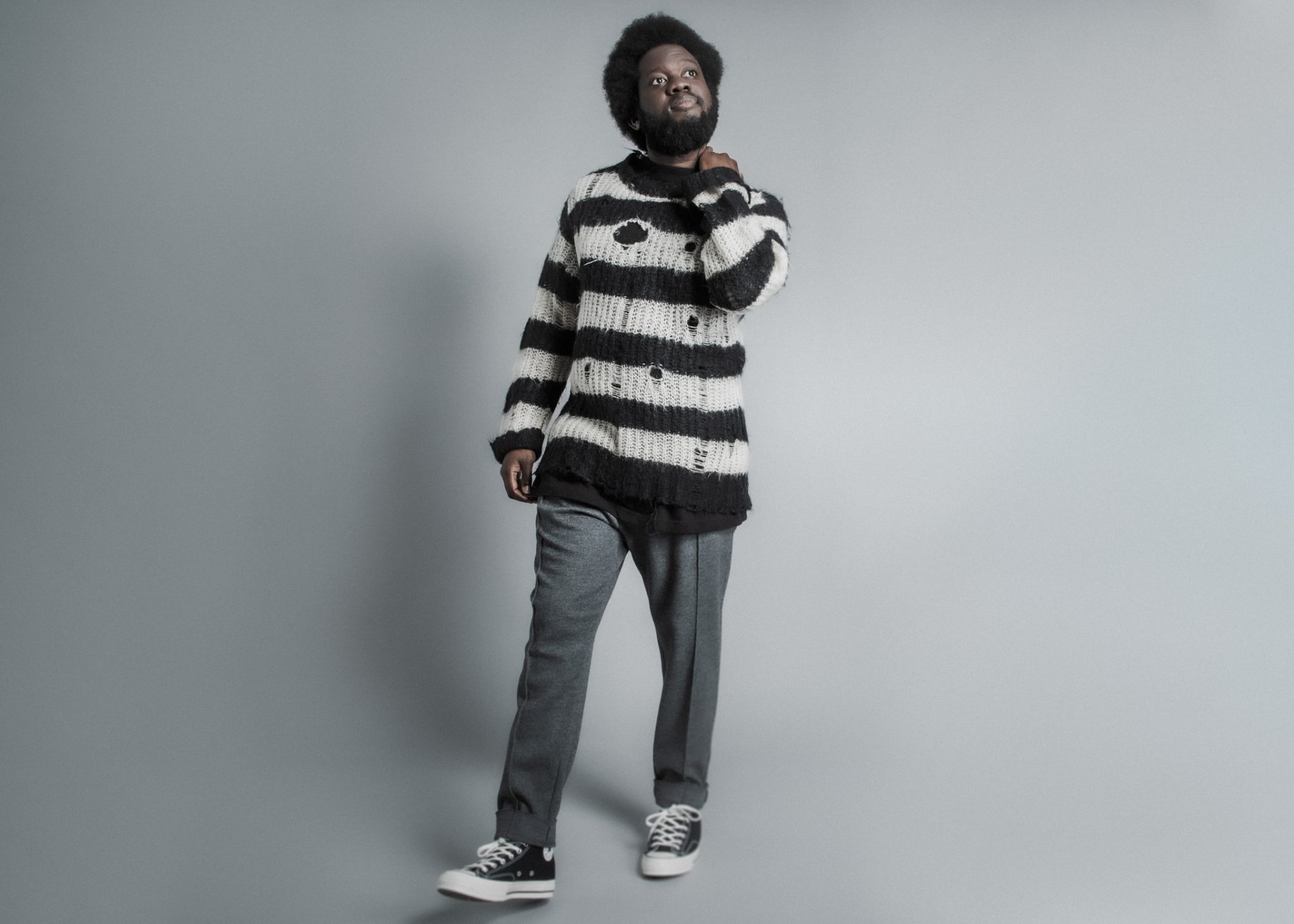 Michael Kiwanuka in a striped sweater posing for an HD desktop wallpaper on a gray background.