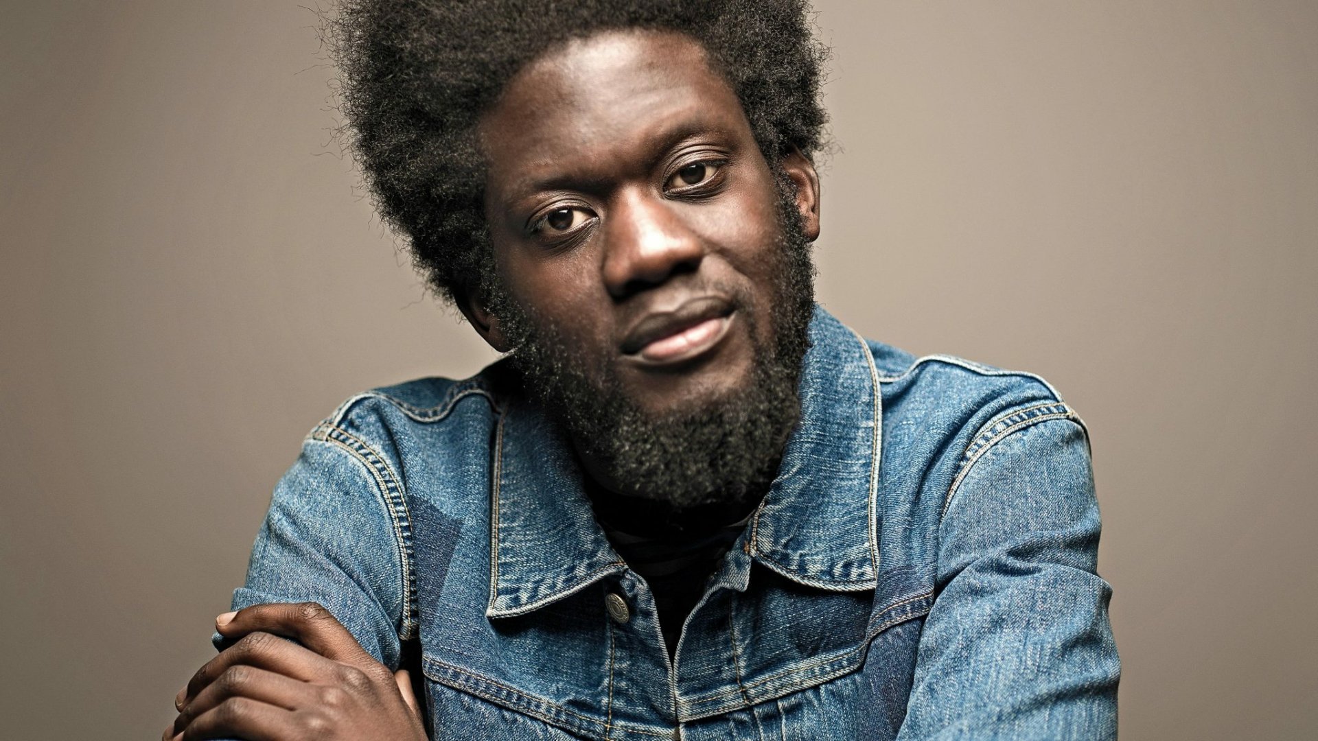 HD desktop wallpaper featuring a portrait of a man in denim, tagged as Michael Kiwanuka, with a neutral background.