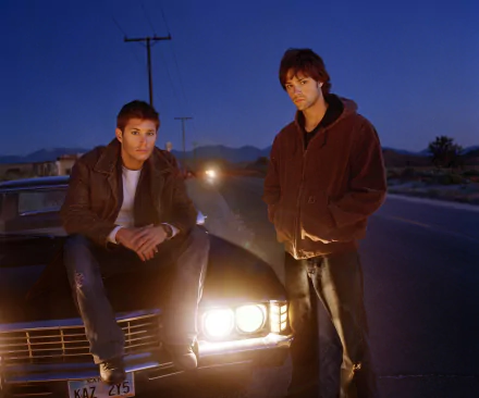 HD desktop wallpaper featuring Jared Padalecki and Jensen Ackles as Sam and Dean Winchester from the TV show Supernatural, standing by a car at dusk.