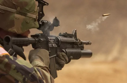 A soldier in full camouflage gear fires an M4 Carbine, captured mid-action with a shell casing in the air. This HD military-themed image serves as a dynamic wallpaper and background.