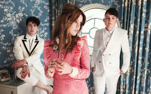 HD desktop wallpaper featuring the band Echosmith with Sydney Sierota in the foreground, standing in a room with vintage wallpaper.