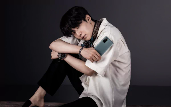 Suga (Min Yoongi) from BTS sits against a dark backdrop, holding a smartphone, captured in a 4K Ultra HD music-themed PC desktop wallpaper.