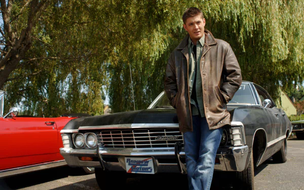 HD PC desktop wallpaper of Dean Winchester (Supernatural) leaning against the black Impala in a leather jacket, framed by willow trees — TV show background.