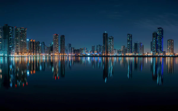 Night view of Sharjah, United Arab Emirates skyline with illuminated skyscrapers reflecting on calm water, captured in stunning 4K Ultra HD.
