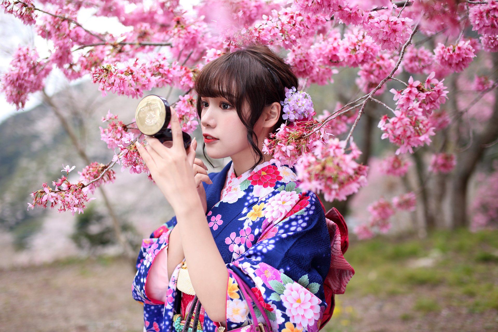Asian woman with brunette hair wearing a floral kimono, surrounded by pink blossom trees, captured in vibrant 4K Ultra HD for a desktop wallpaper.