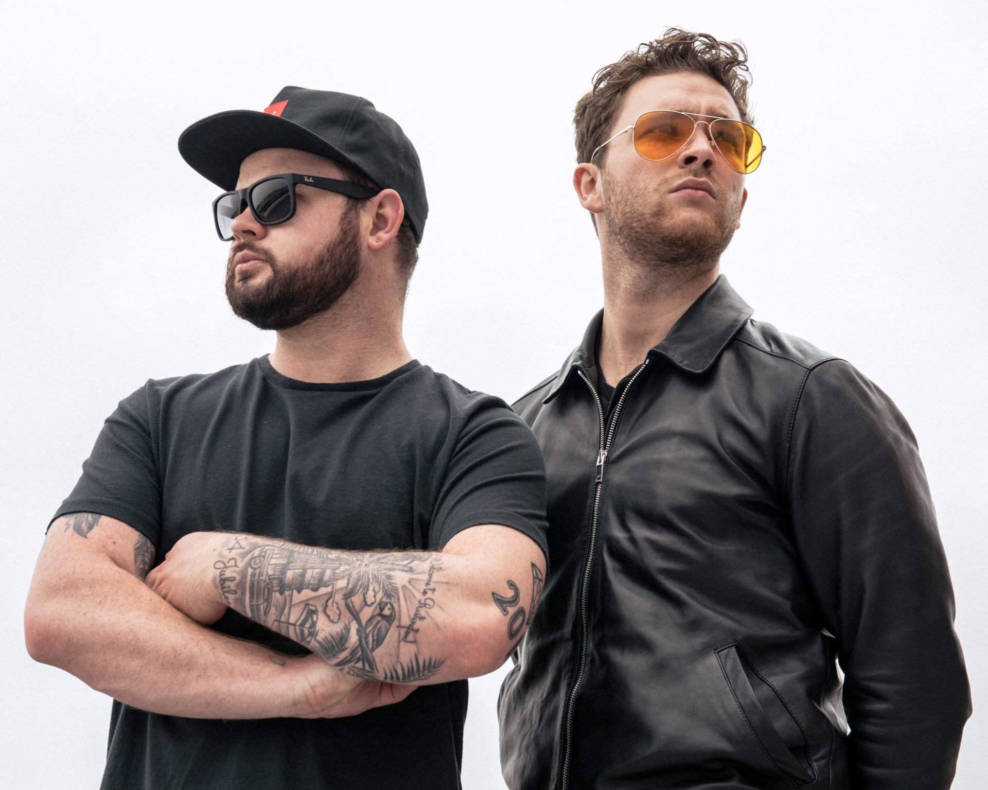 HD wallpaper featuring two confident men associated with Royal Blood, one with tattoos and a cap, the other with sunglasses and a leather jacket, against a clear background.