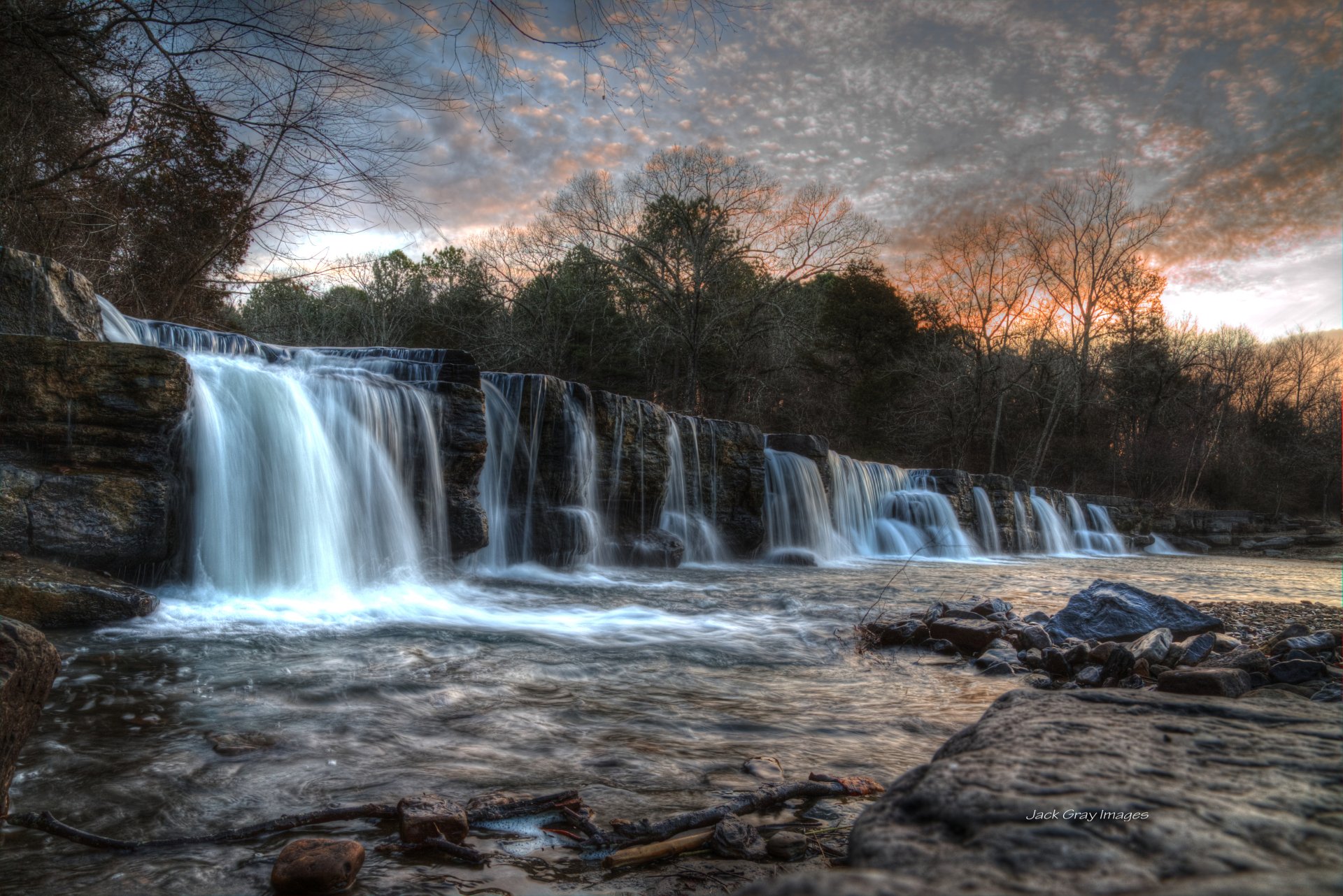 A stunning 4K Ultra HD waterfall cascading over rocks surrounded by trees under a dramatic sky, showcasing the beauty of water and nature.