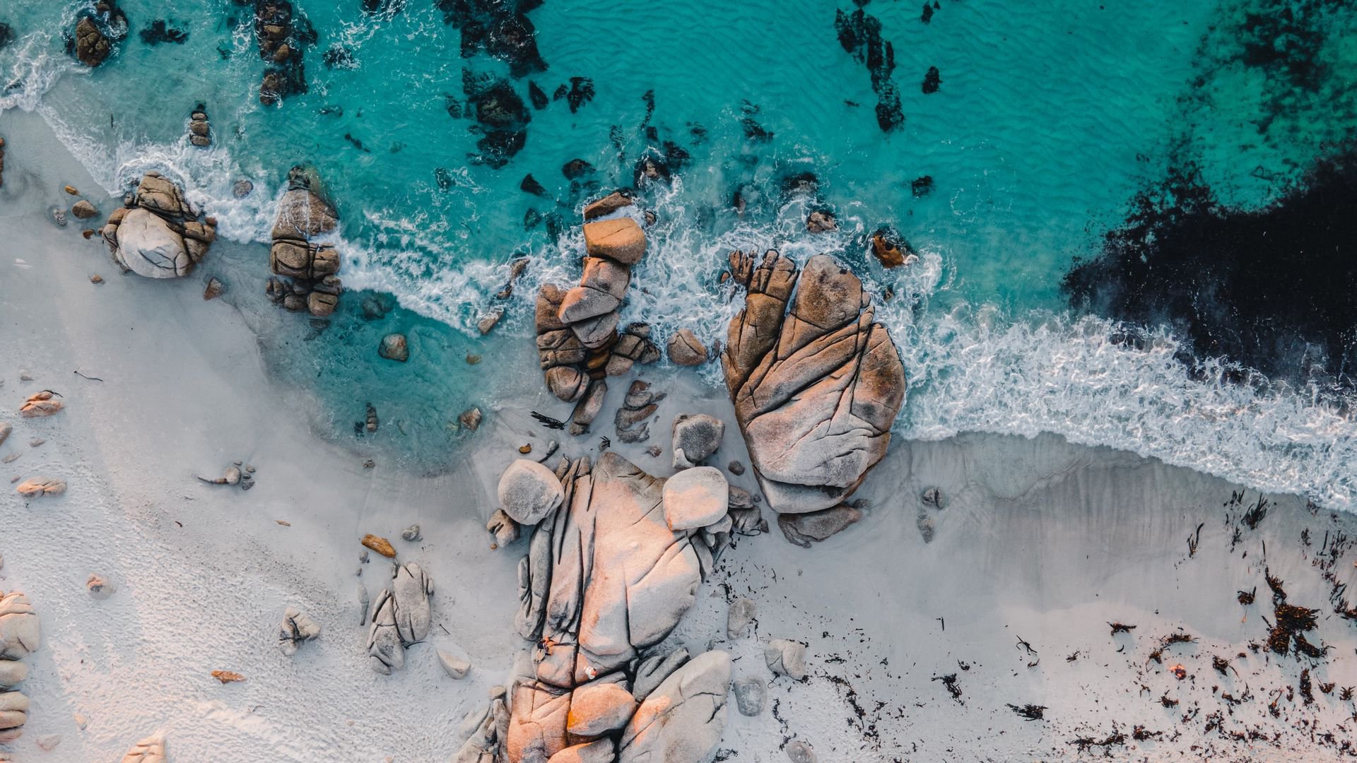 Aerial view of a serene beach featuring smooth rocks, turquoise waters, and gentle waves, showcasing the beauty of nature in this HD desktop wallpaper.