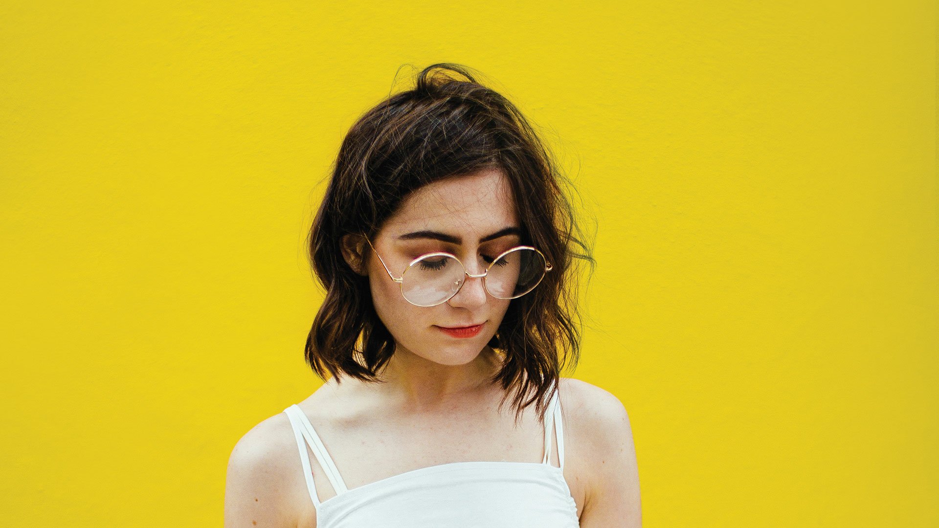 Young woman with glasses against a vibrant yellow background, poised for a stylish HD desktop wallpaper. Tagged with dodie.
