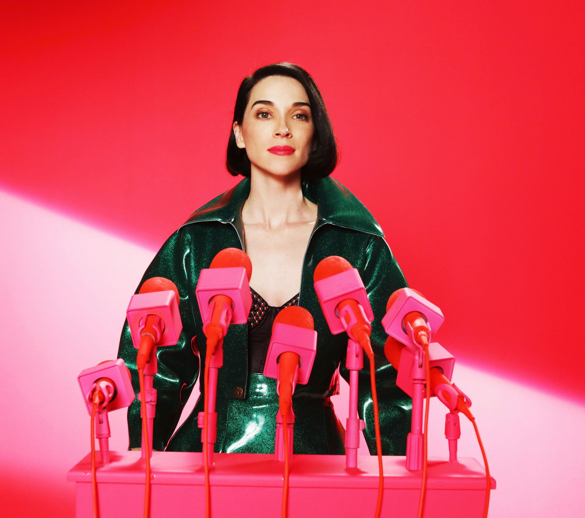 HD desktop wallpaper featuring a styled individual in a green jacket surrounded by pink microphones against a vibrant red background, tagged with St. Vincent.