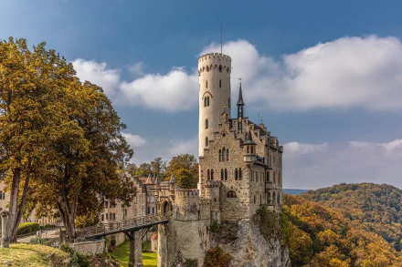 Lichtenstein Castle in Württemberg, Germany, perched atop a rocky cliff surrounded by autumn trees under a bright blue sky.