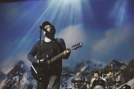 HD desktop wallpaper featuring a Fall Out Boy band member playing guitar on stage with dramatic lighting and a mountainous backdrop.
