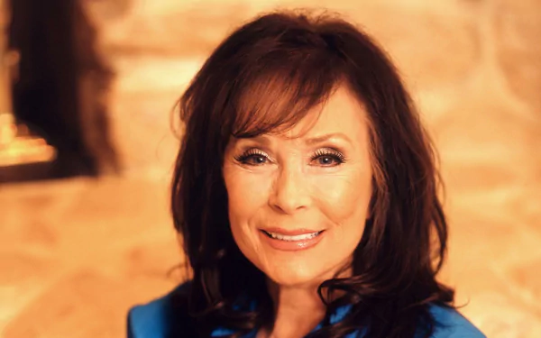 HD desktop wallpaper featuring a portrait of a smiling woman in a blue top, tagged with Loretta Lynn, with a warm-toned background.