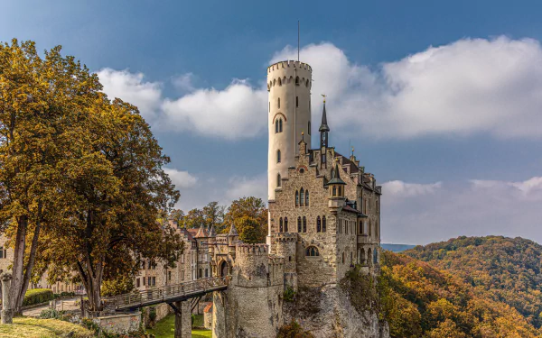 Lichtenstein Castle in Württemberg, Germany, perched atop a rocky cliff surrounded by autumn trees under a bright blue sky.